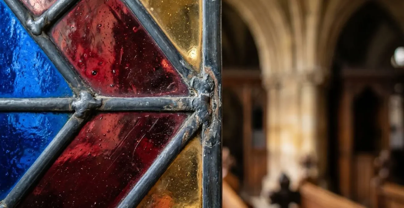 Détail de vitrail Renaissance dans une chapelle historique avec jeux de lumière colorée traversant le verre ancien